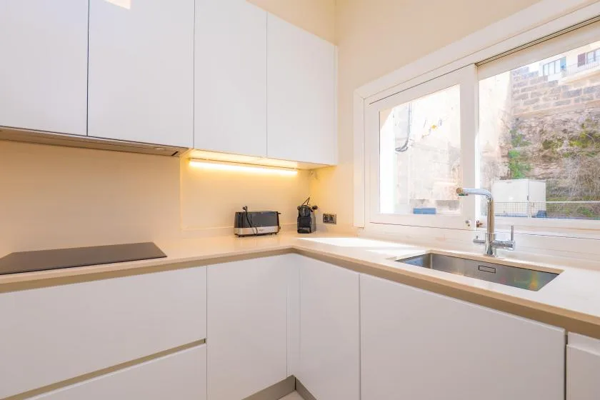 A bright kitchen with white cabinets, a countertop, and a sink by the window.