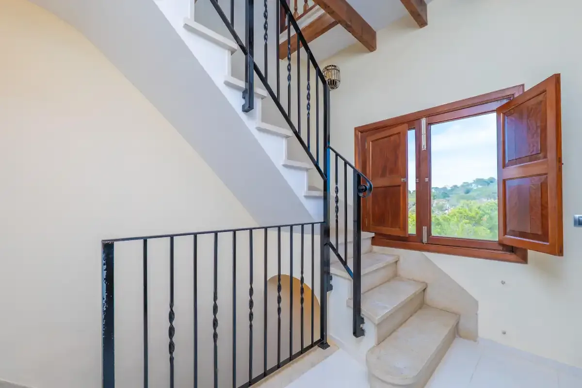 A stairway with a black railing beside an open wooden window.