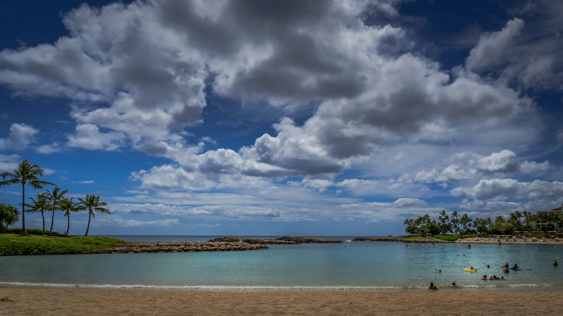 Una laguna costera tranquila con bañistas bajo un cielo nublado.