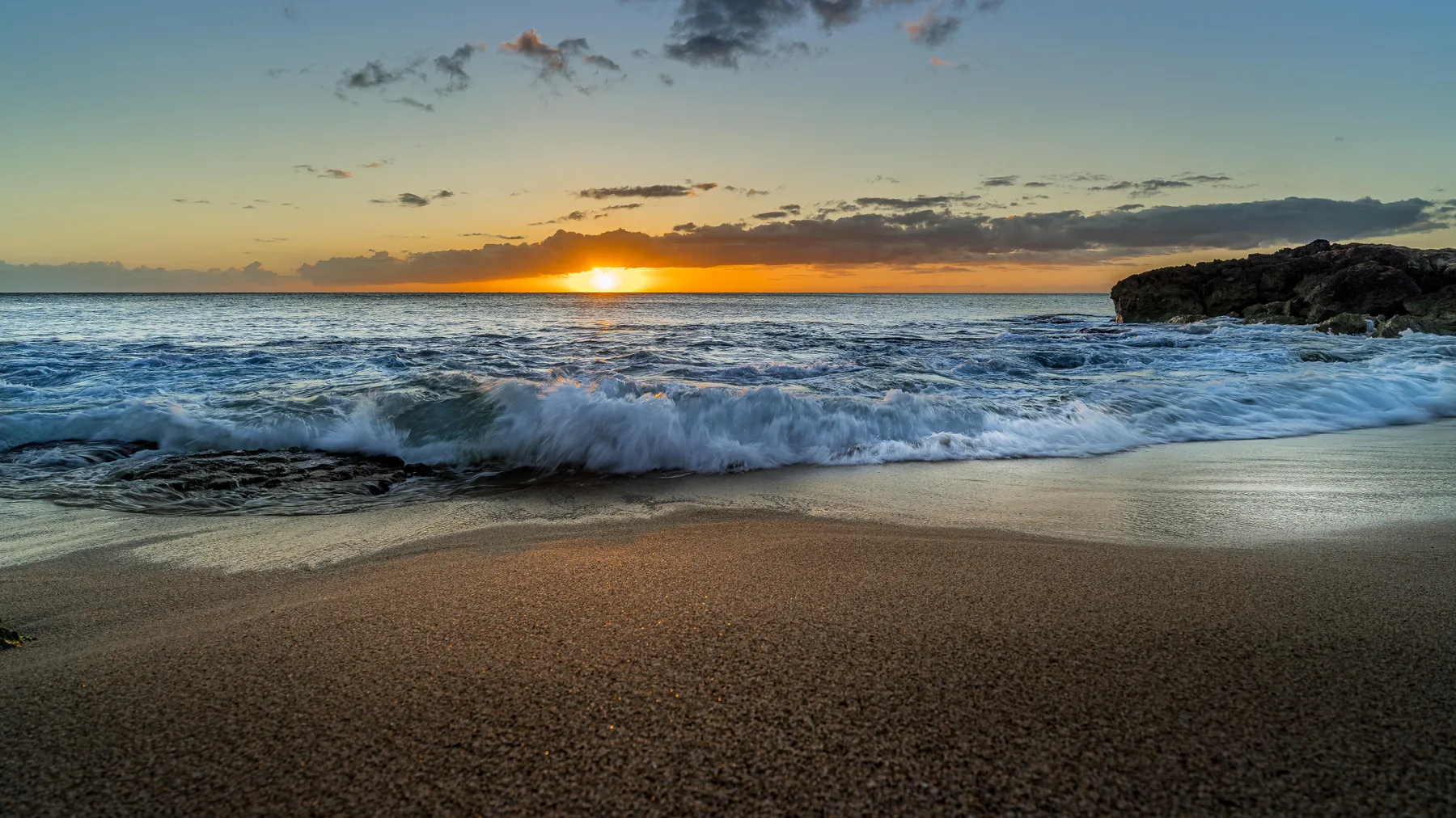 Atardecer sobre olas del océano que llegan a una playa de arena.
