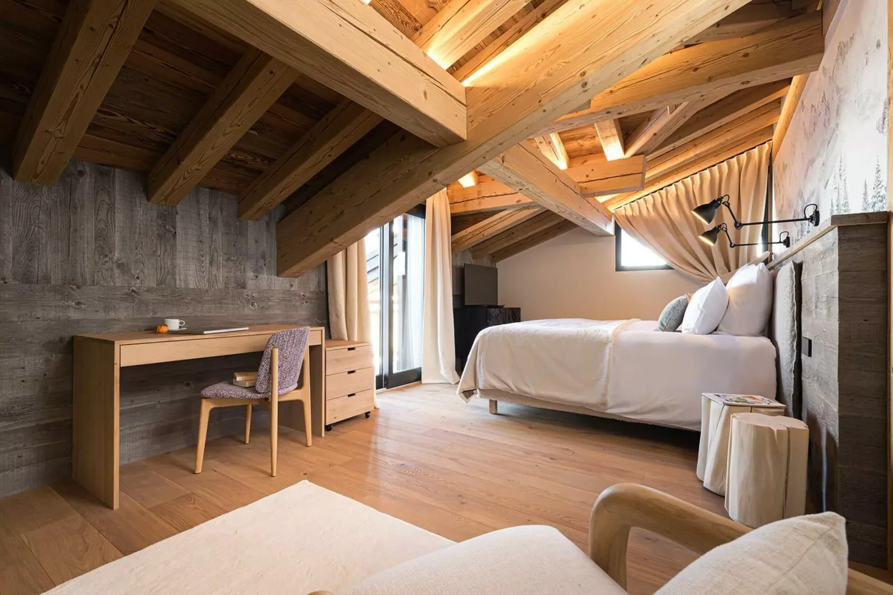 A bedroom with a bed, desk, and exposed wooden ceiling.