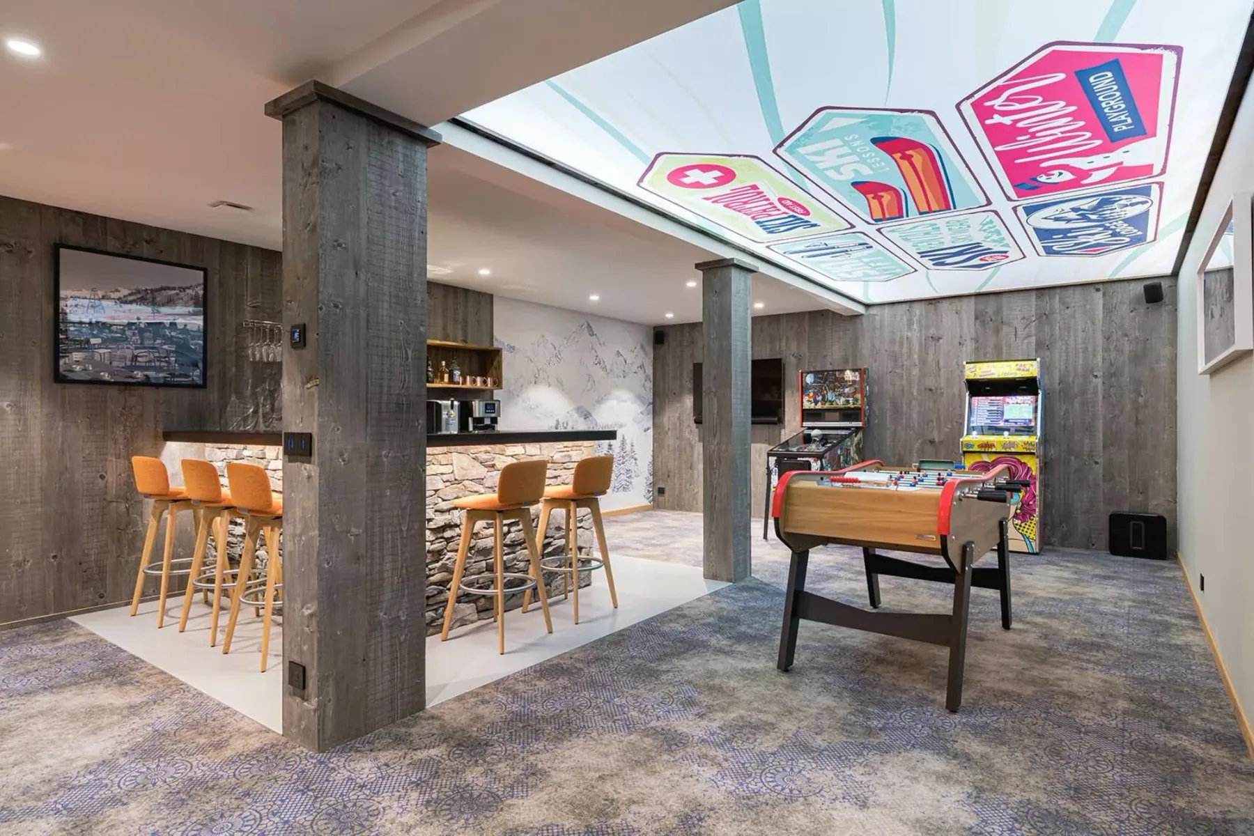 A game room with a foosball table, arcade games, and a bar area.