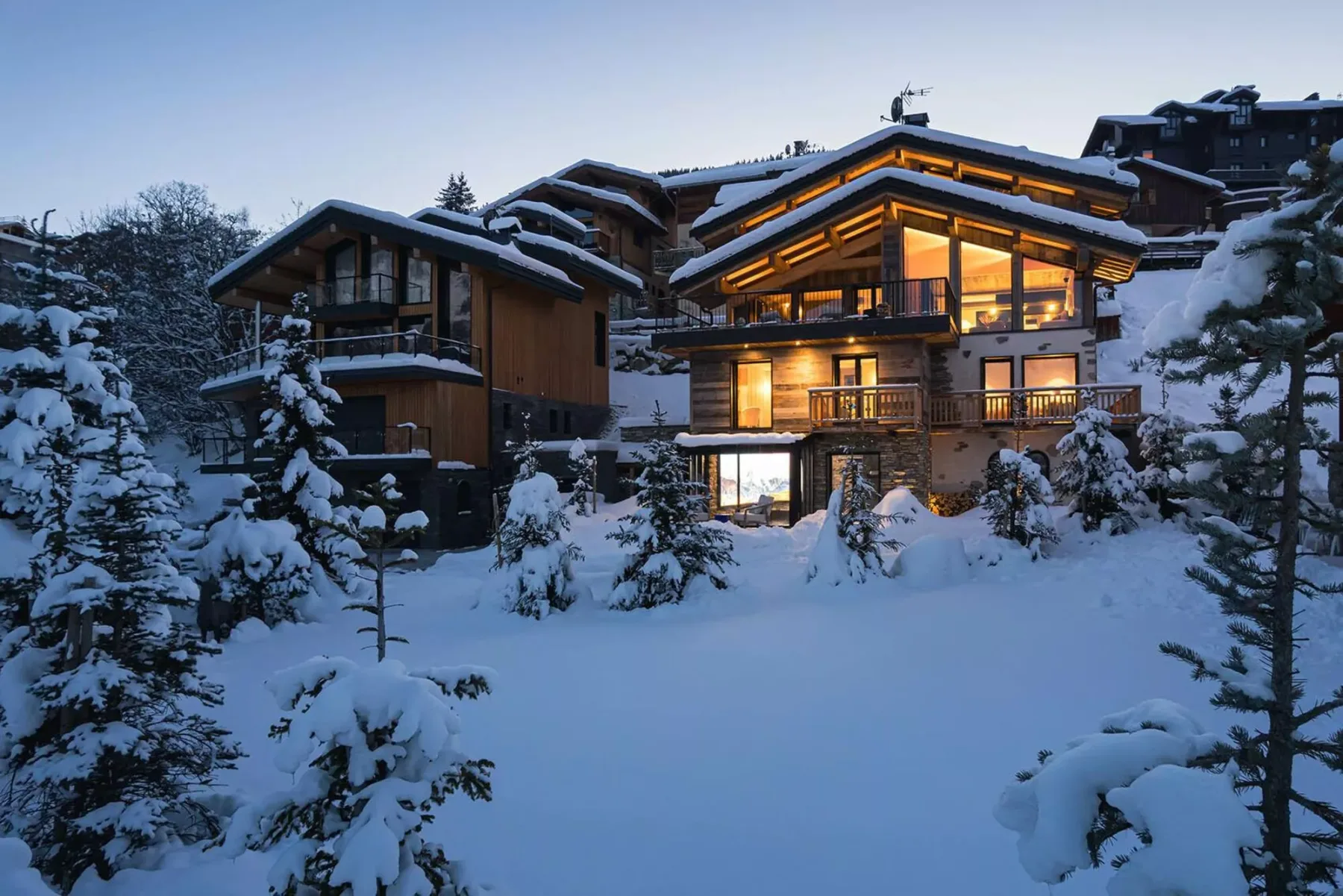 A chalet-style building glows warmly amid snow-covered trees at dusk.