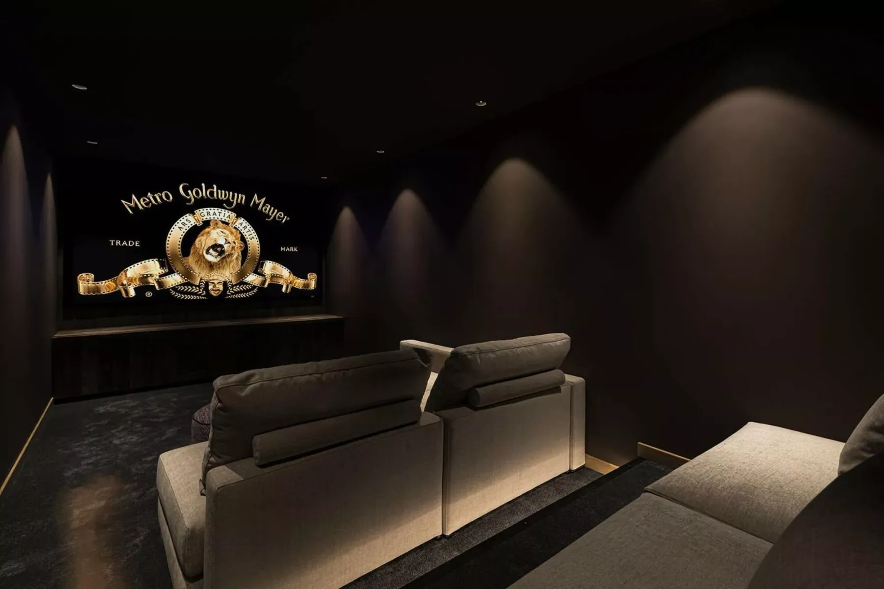 A dark home theater features cushioned seating facing a movie screen.