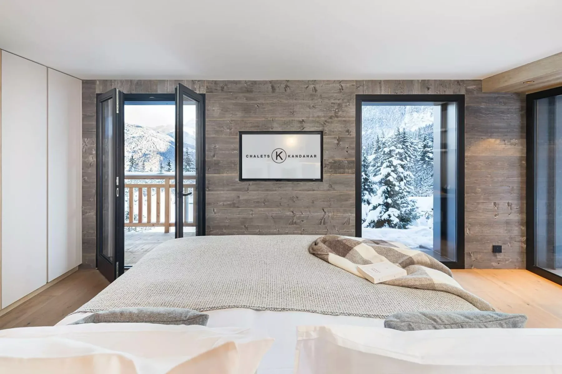 A bedroom with a large bed, wood-paneled walls, and snowy mountain views through the windows.