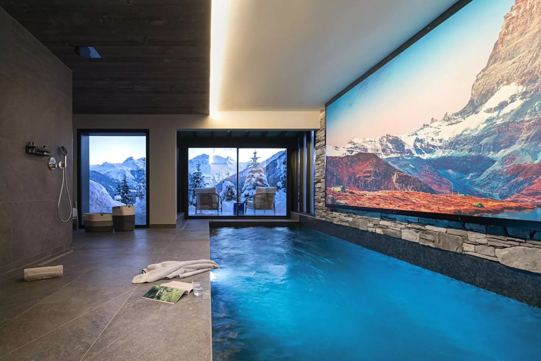 An indoor pool beside large windows overlooks a snowy mountain landscape.