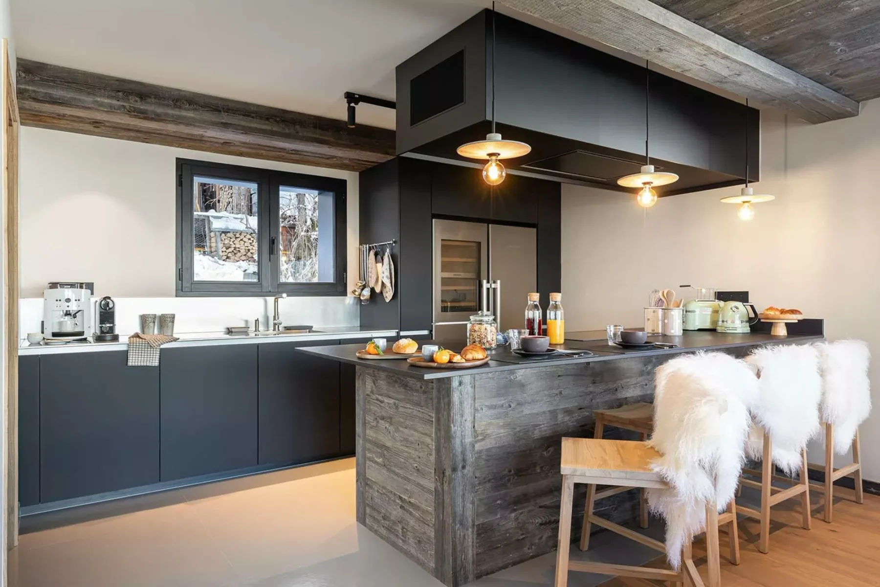 A modern kitchen with a dark island, countertop seating, and pendant lights.