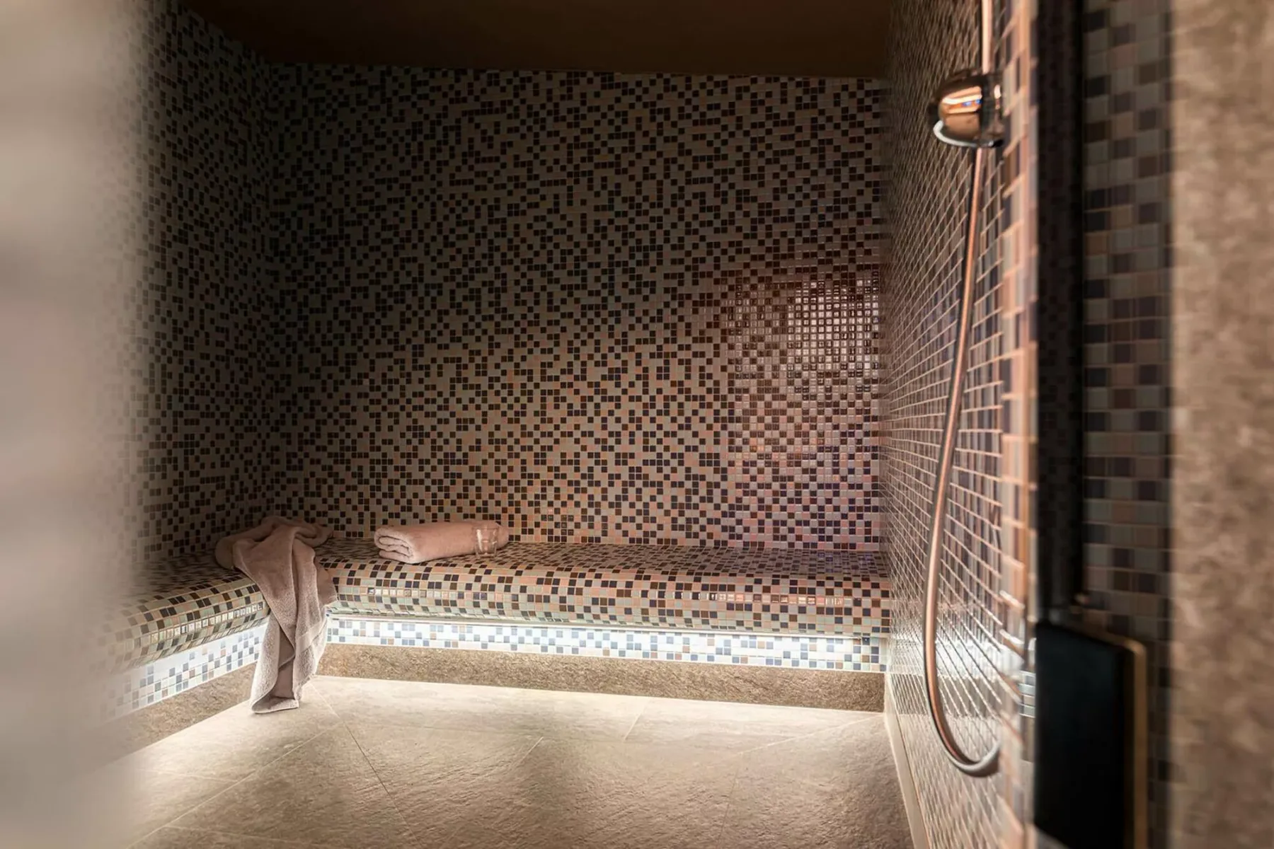 A tiled shower area with a handheld showerhead and a towel draped nearby.
