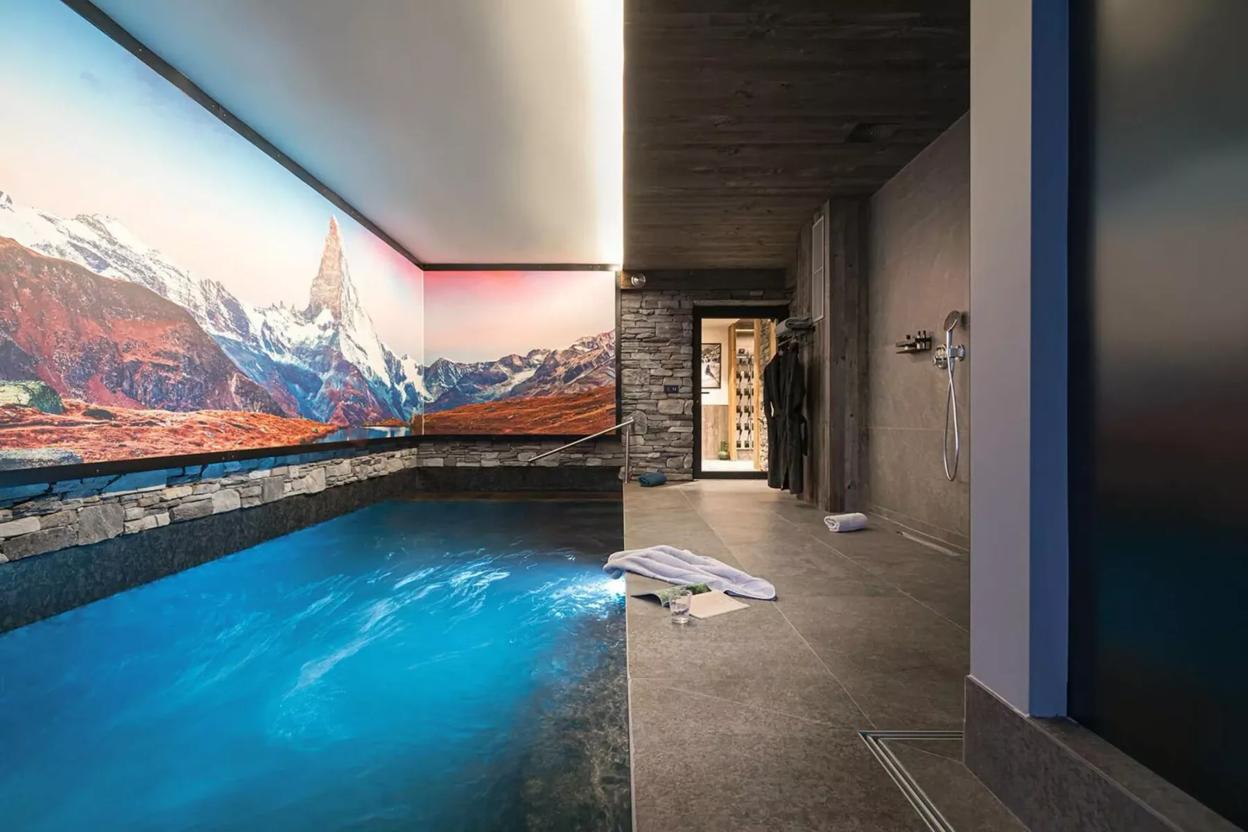 An indoor pool beside a tiled walkway, with a mountain mural along the wall.