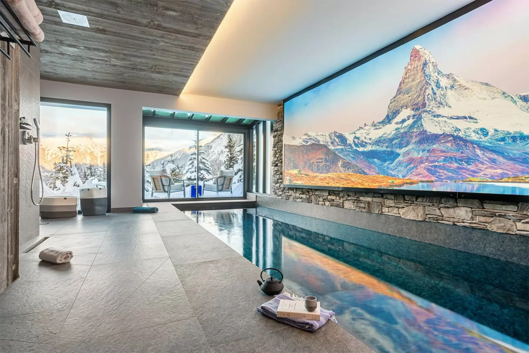 An indoor swimming pool sits beside large windows and a wall-sized mountain image.