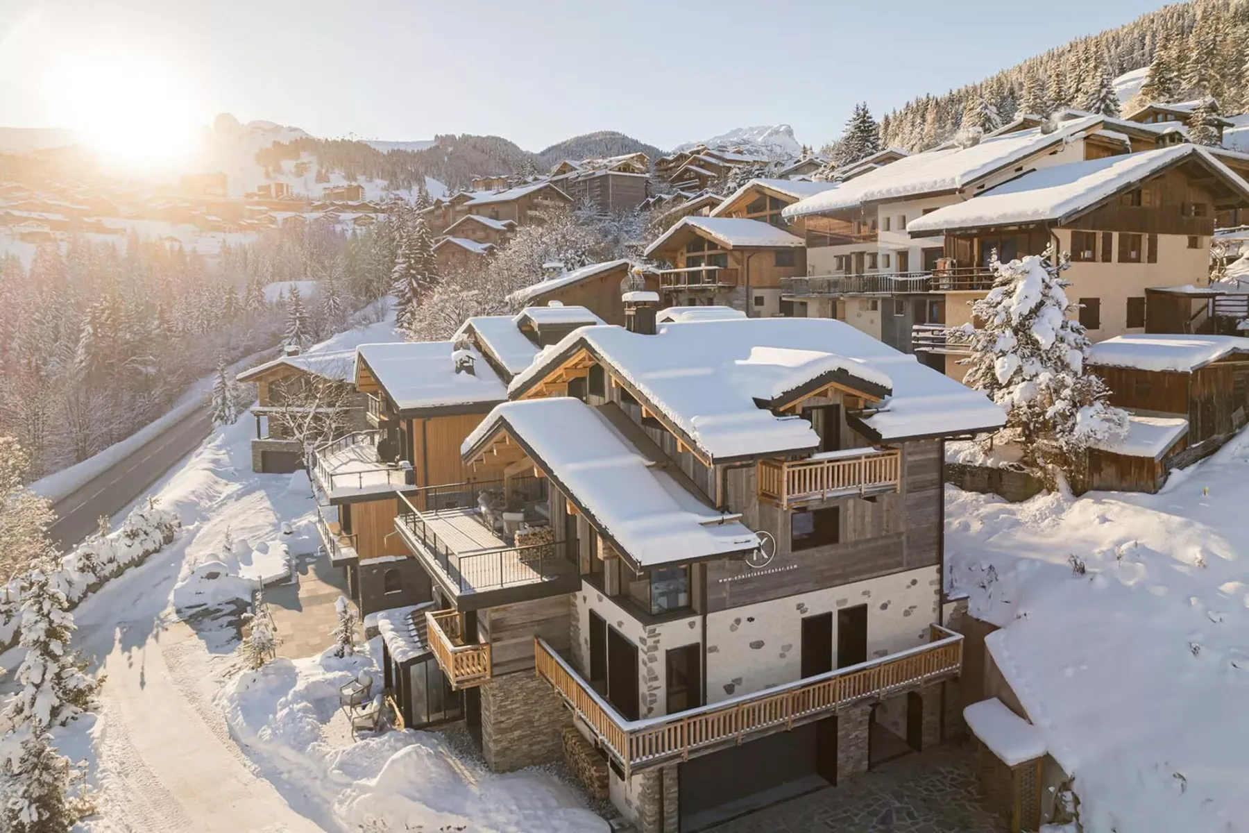 Snow-covered mountain chalets cluster along a winding road in winter sunlight.