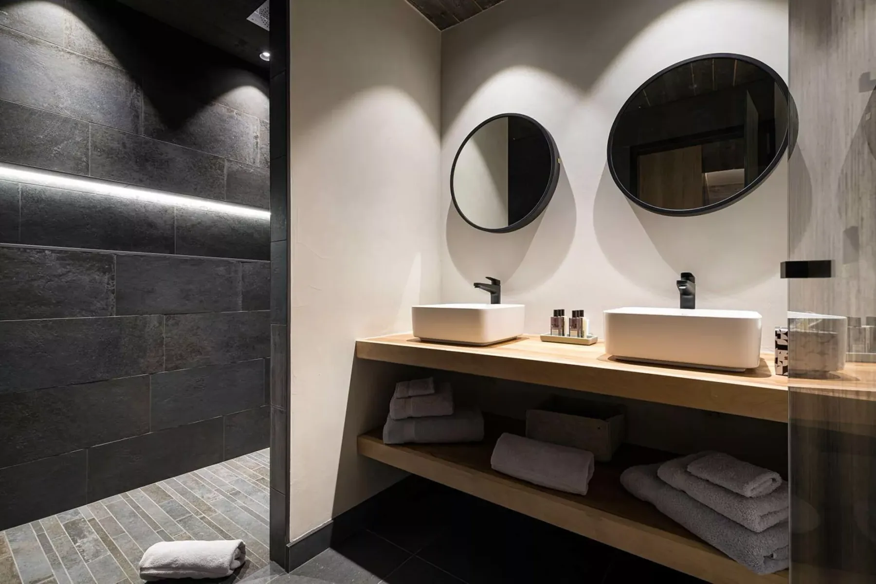 A modern bathroom with a double vanity, round mirrors, and a tiled shower.
