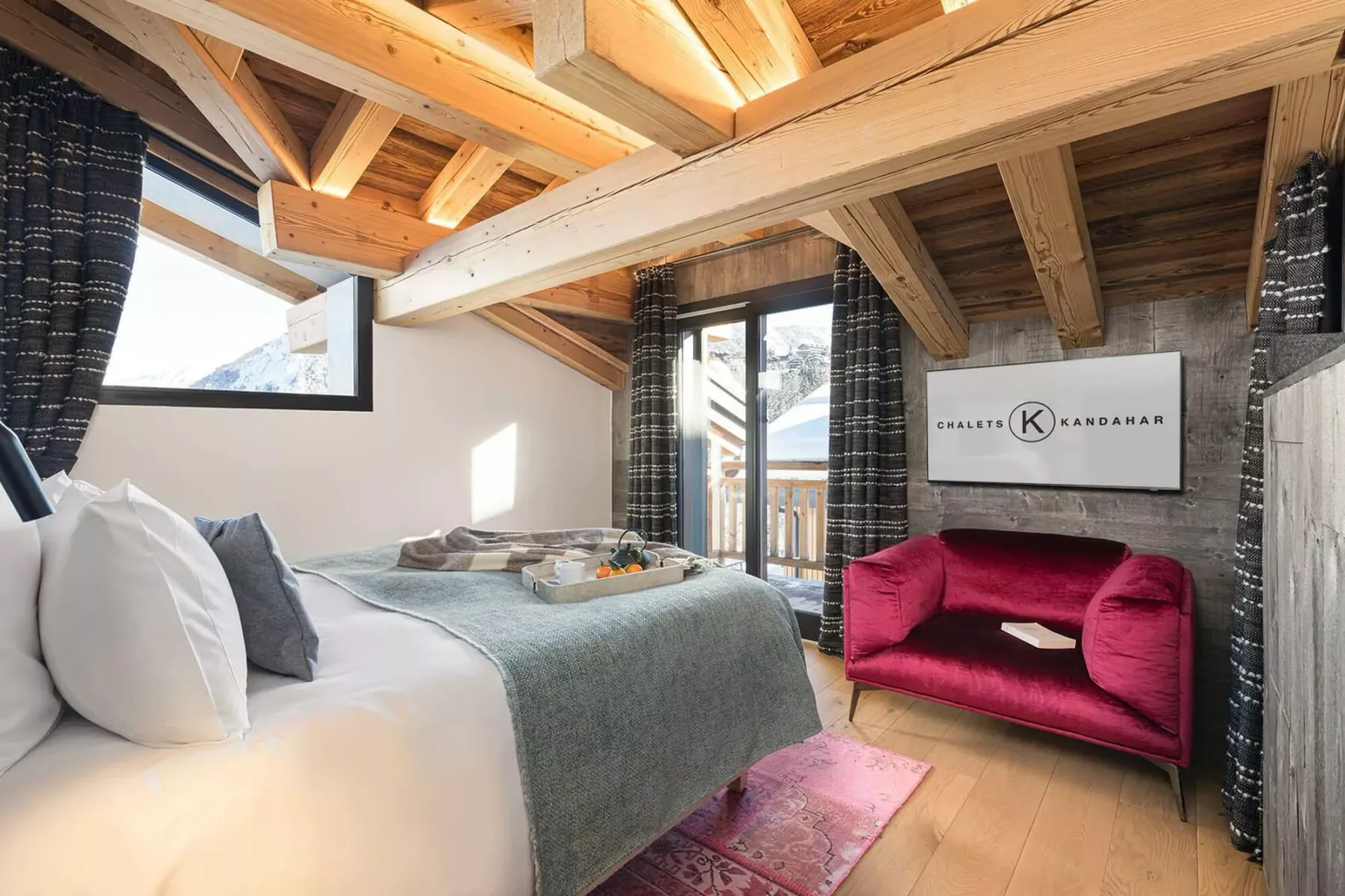 A bedroom with a bed, a red loveseat, and exposed wooden ceiling beams.