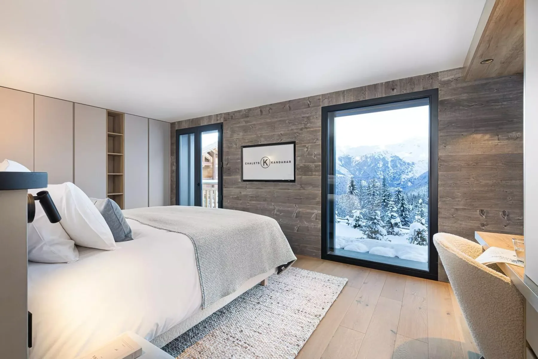 A bedroom with a large bed beside windows overlooking a snowy mountain landscape.