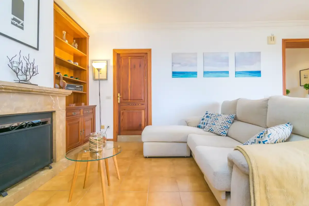 Una sala de estar con asientos claros, una chimenea y una mesa de centro de vidrio.