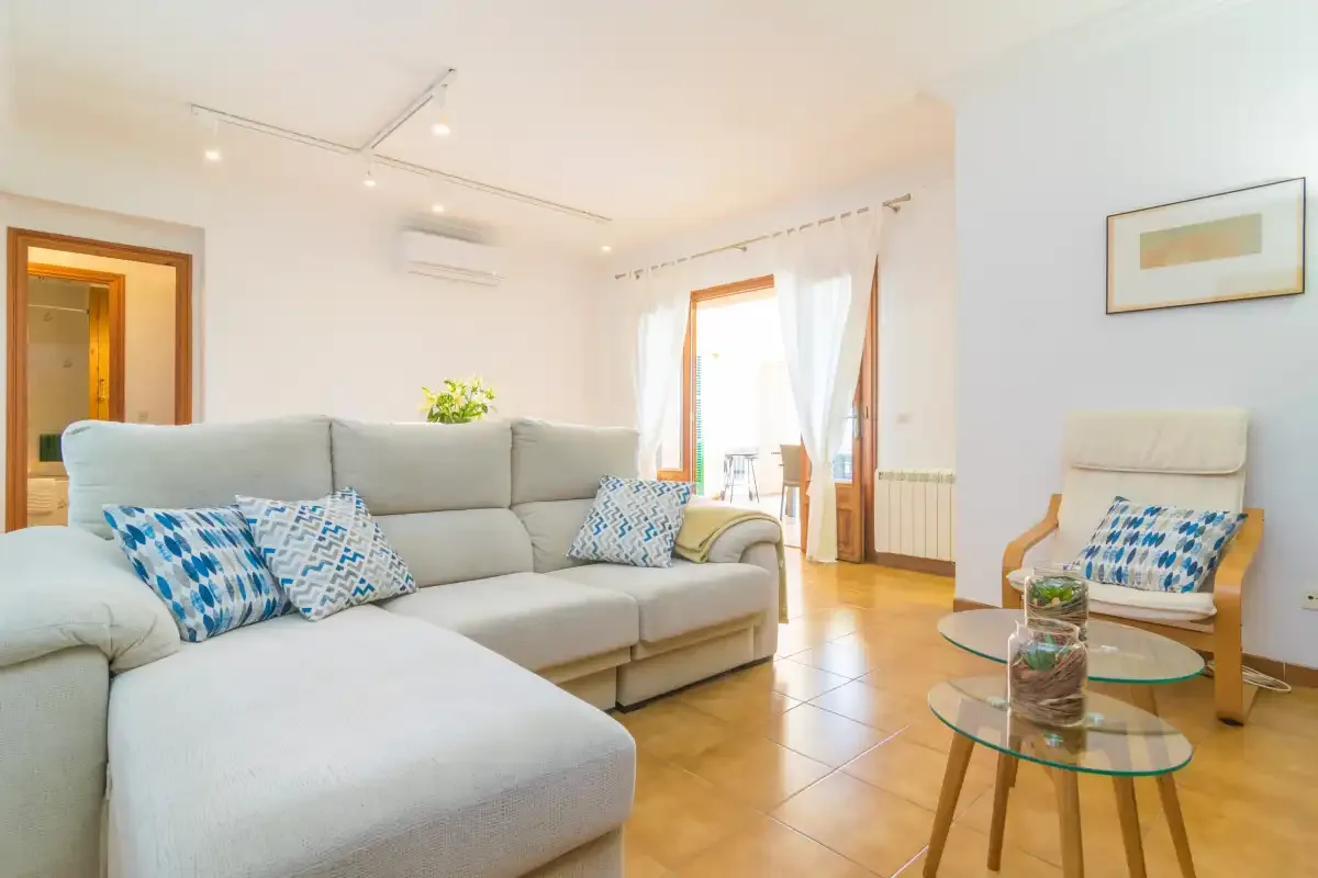 Una sala luminosa con un sofá seccional y una mesa de centro de vidrio.