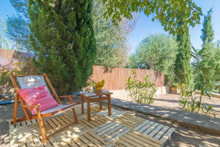 Una zona de estar al aire libre a la sombra, con una mesa baja entre árboles y plantas.