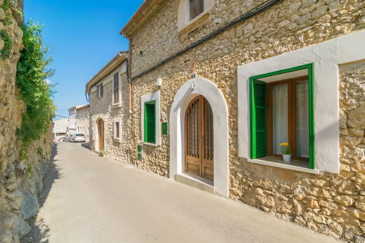 Una calle estrecha junto a edificios de piedra con contraventanas verdes.