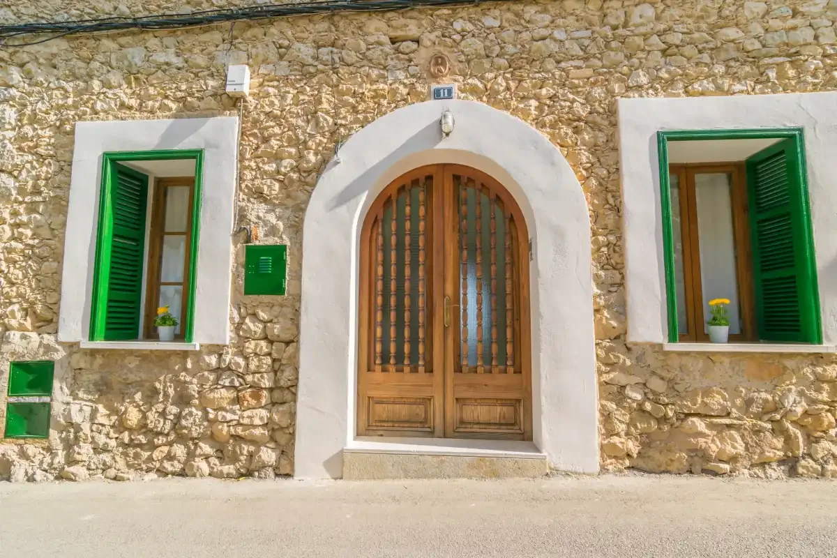 Fachada de piedra con una entrada arqueada de madera y contraventanas verdes.