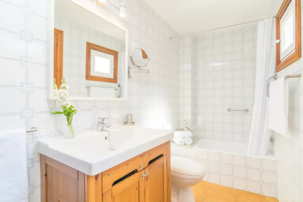 Un baño luminoso con azulejos, lavabo, espejo e inodoro.