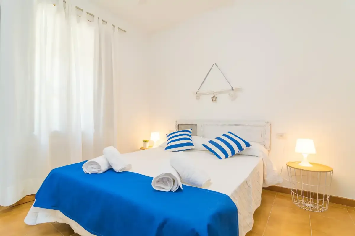 Un dormitorio luminoso con una cama vestida con ropa de cama azul y blanca.