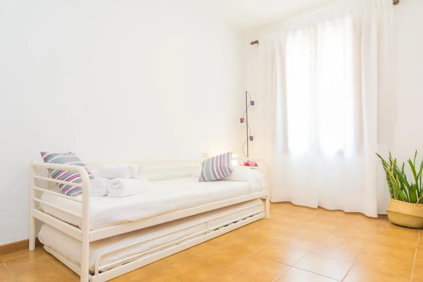 Un dormitorio luminoso con una cama nido blanca, cojines a rayas y una ventana con cortinas.