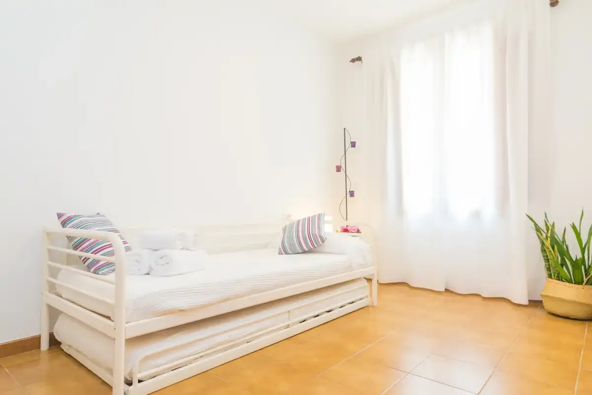 Una habitación luminosa con un diván blanco junto a una gran ventana con cortinas.
