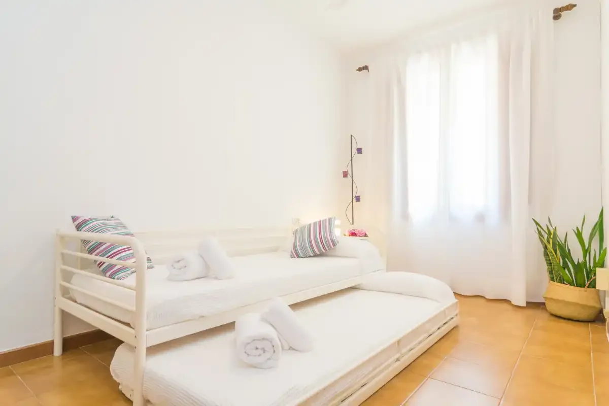 Un dormitorio luminoso con dos camas blancas y cortinas translúcidas.