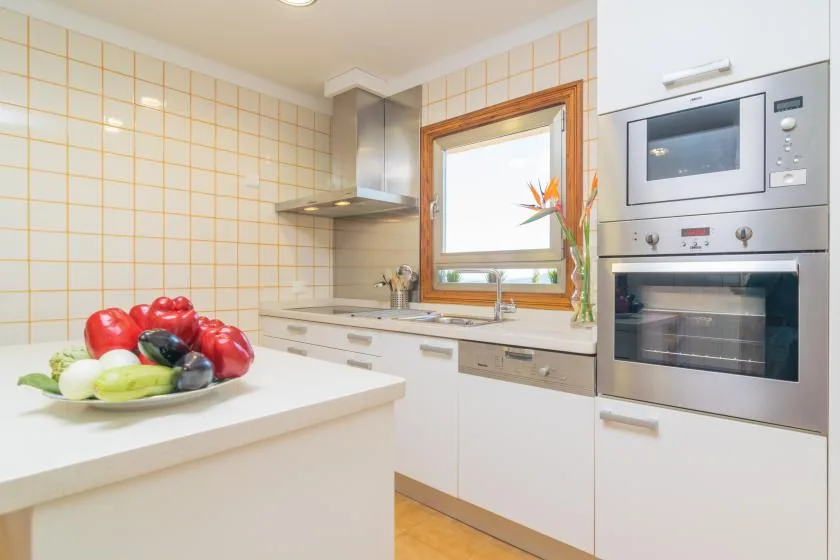 Una cocina luminosa con armarios blancos, paredes alicatadas y una ventana sobre el fregadero.