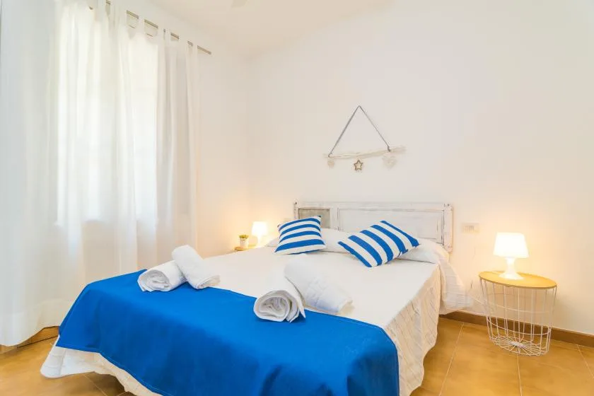 Un dormitorio luminoso con una colcha azul y almohadas a rayas.
