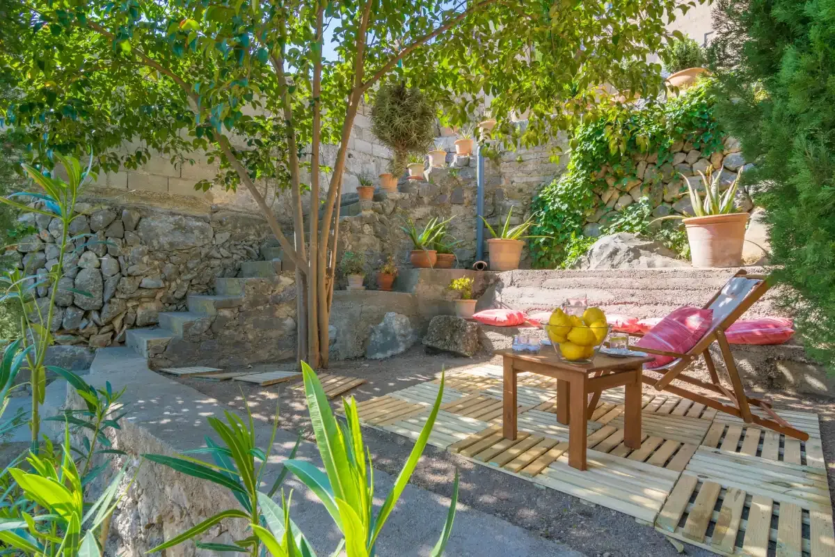 Un patio ajardinado a la sombra, con asientos al aire libre y plantas en macetas.