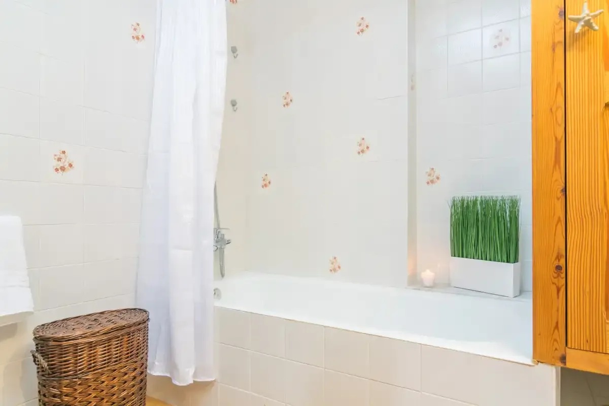 Un baño alicatado con bañera, cortina de ducha y cesta de mimbre.