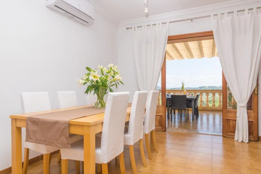 Un comedor luminoso se abre a un balcón, con una mesa y asientos blancos.