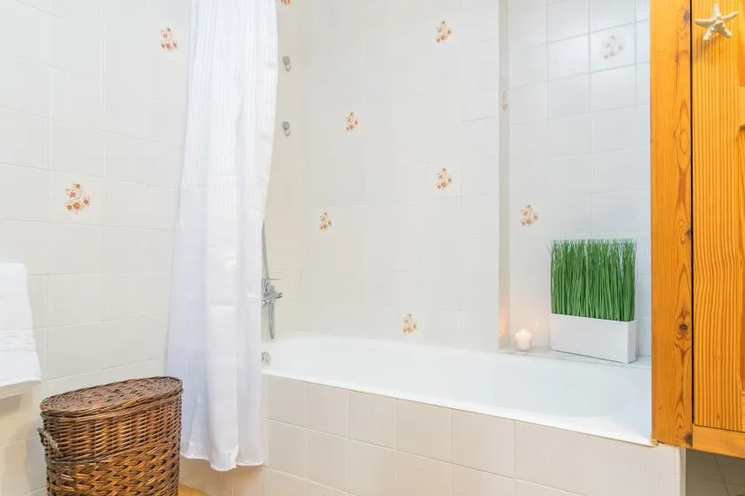 Un baño alicatado cuenta con una bañera, una cortina de ducha blanca y una pequeña planta en una maceta.