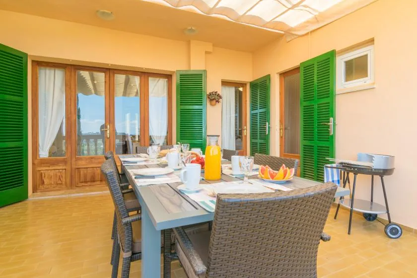 Un comedor en un patio cubierto con una mesa larga preparada para comer.