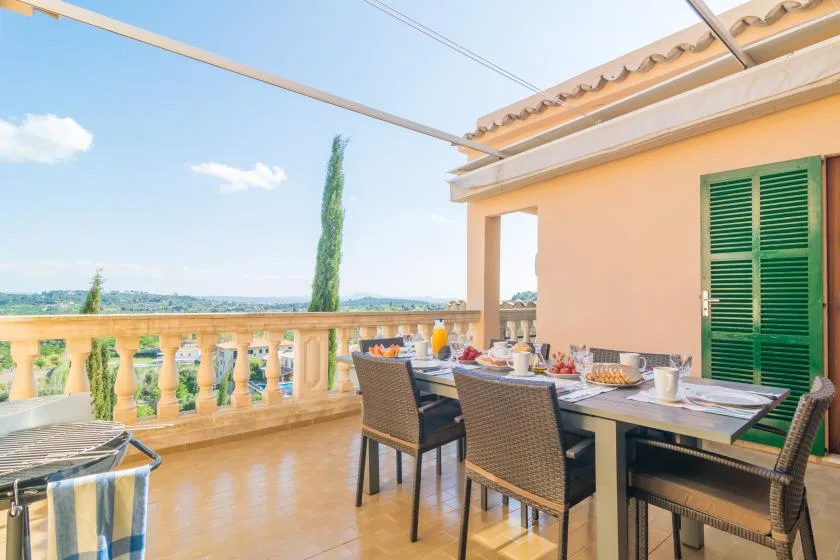 Una zona de comedor en una terraza, junto a persianas verdes y una balaustrada.