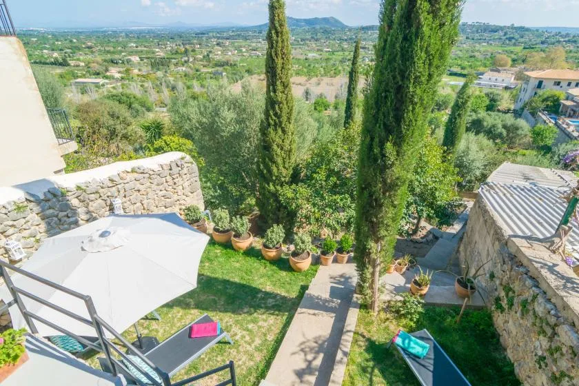 Una terraza ajardinada ofrece vistas a un valle verde, con árboles altos y asientos al aire libre.