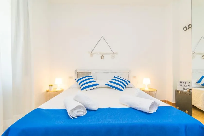 Un dormitorio con ropa de cama blanca, detalles azules y lámparas de noche.