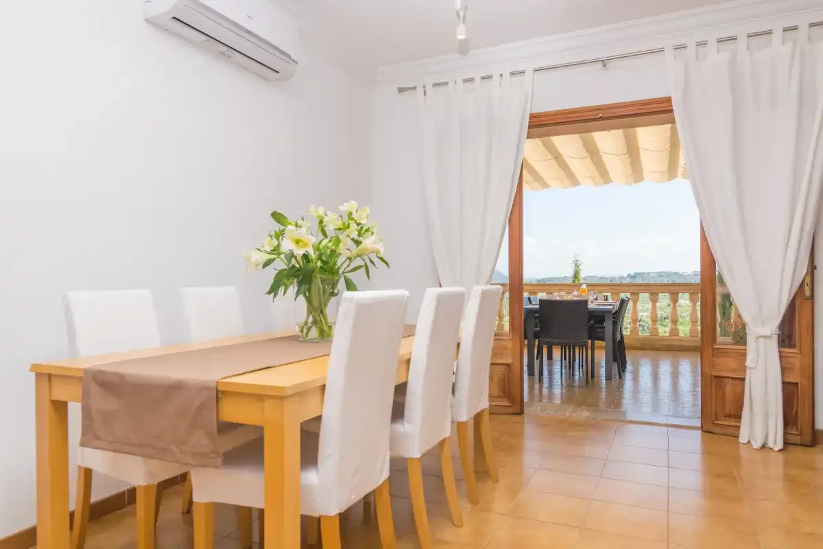 Comedor con mesa y sillas junto a una puerta abierta al balcón.