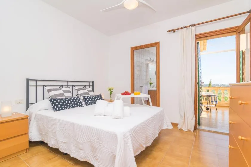 Dormitorio luminoso con una cama bien hecha y la puerta del balcón abierta.