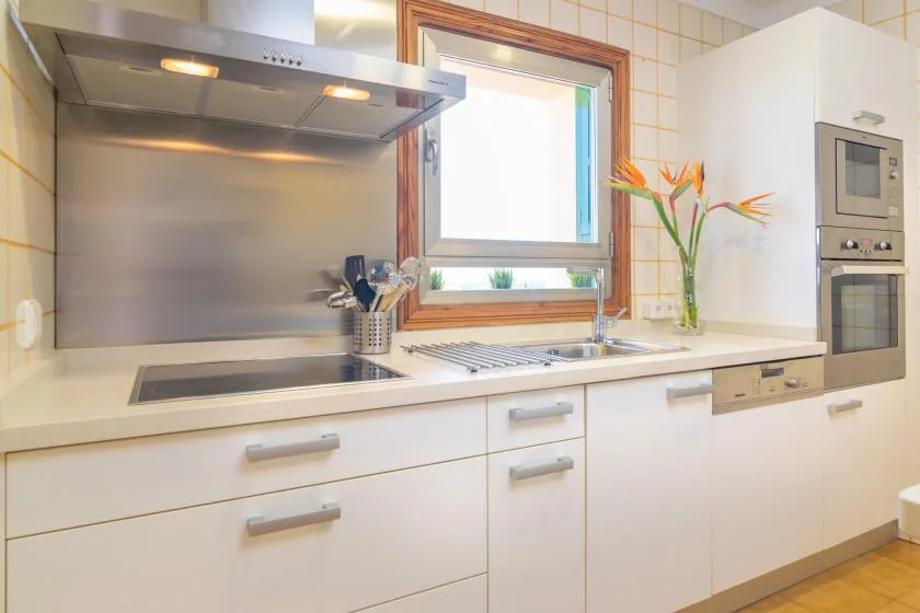 Una cocina luminosa con armarios blancos, una placa de cocina y un fregadero bajo la ventana.