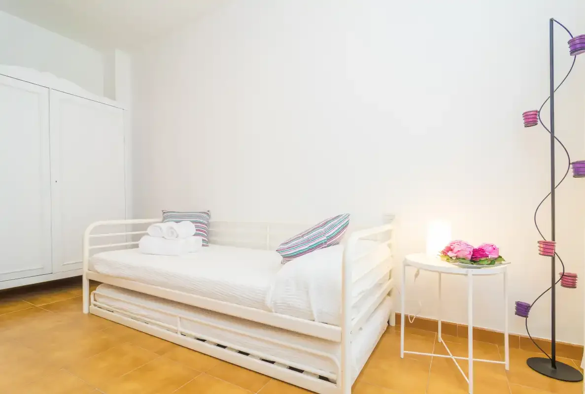 Un dormitorio luminoso con una cama blanca y una mesita de noche.