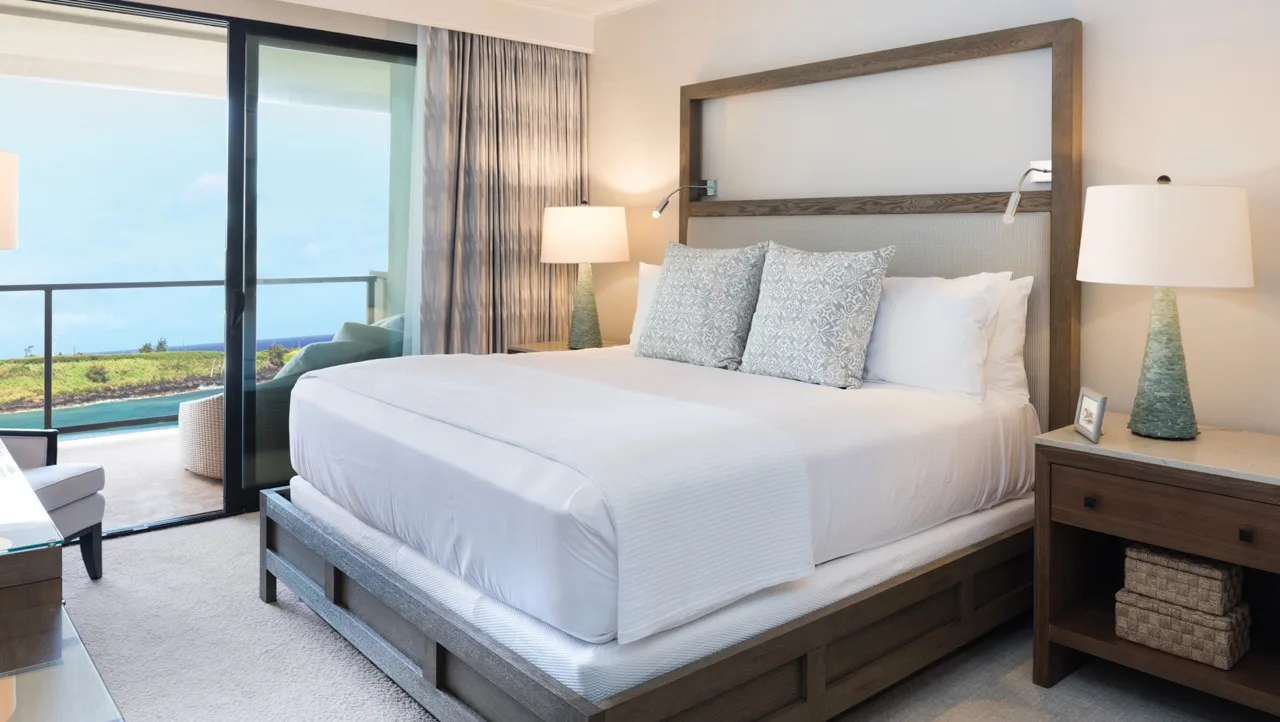 A bright bedroom with a large bed beside sliding glass doors.