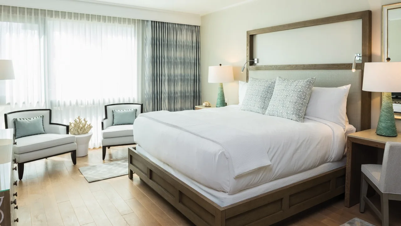 A bright bedroom with a large bed and two armchairs beside the window.