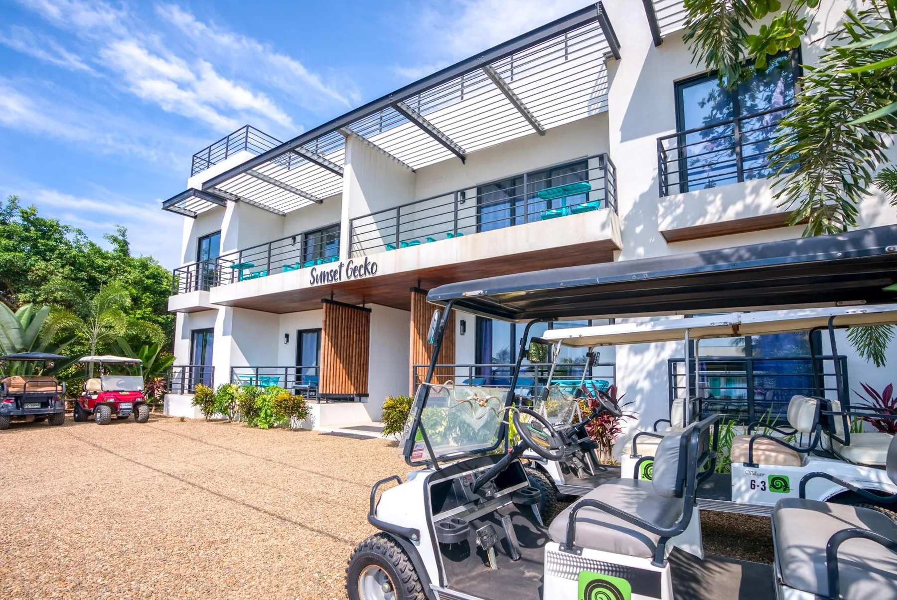 A modern white building with balconies and several golf carts parked outside.