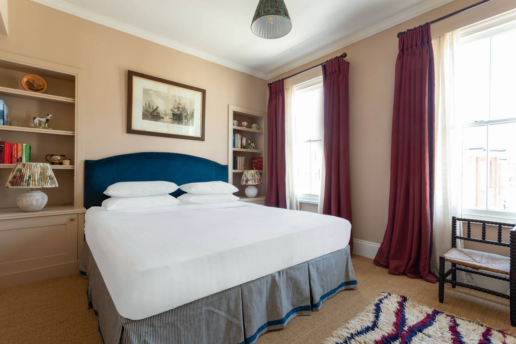 A bedroom with a neatly made bed, burgundy curtains, and built-in shelving.