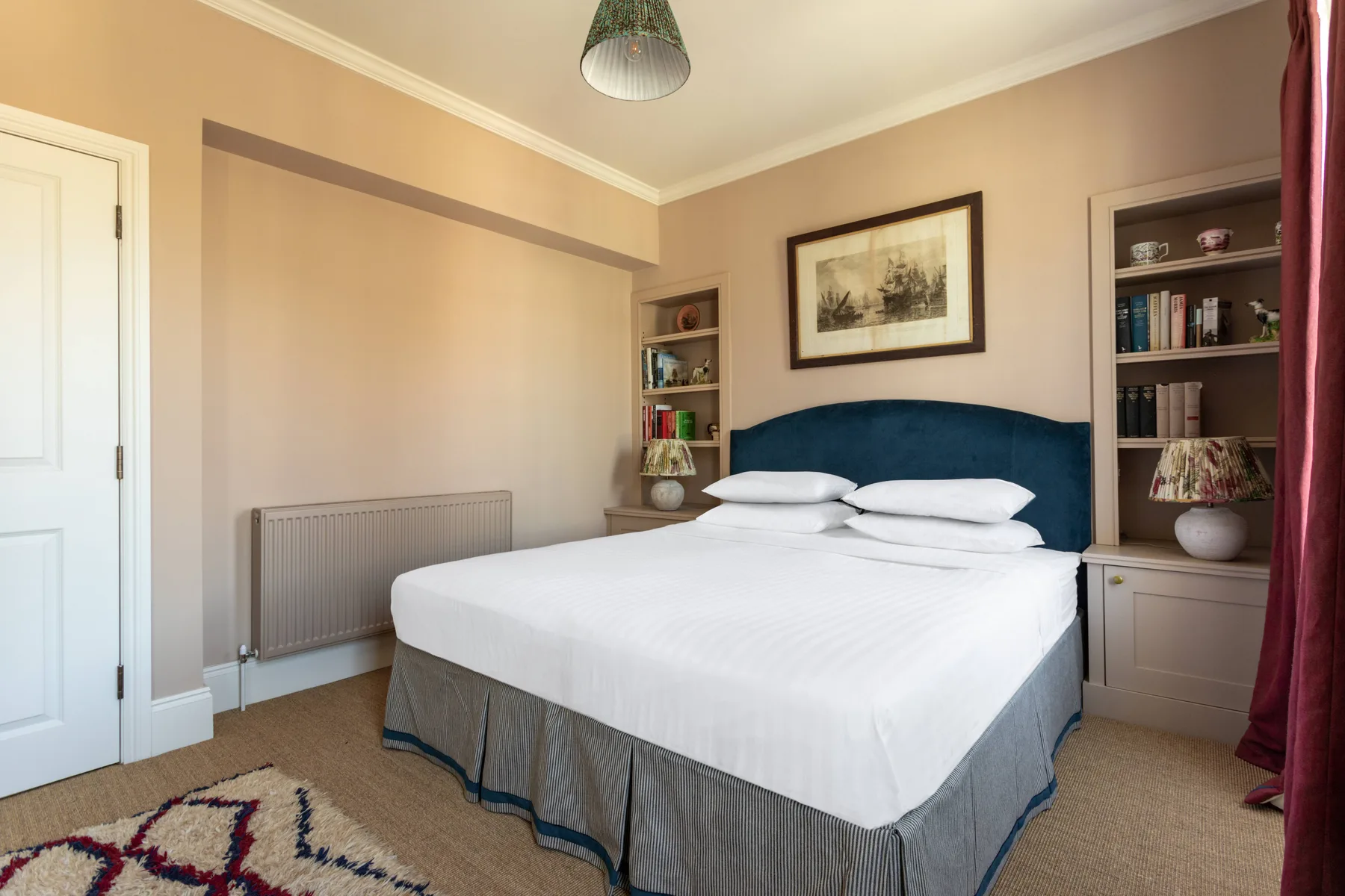 A bedroom with a neatly made bed, built-in shelving, and framed artwork.