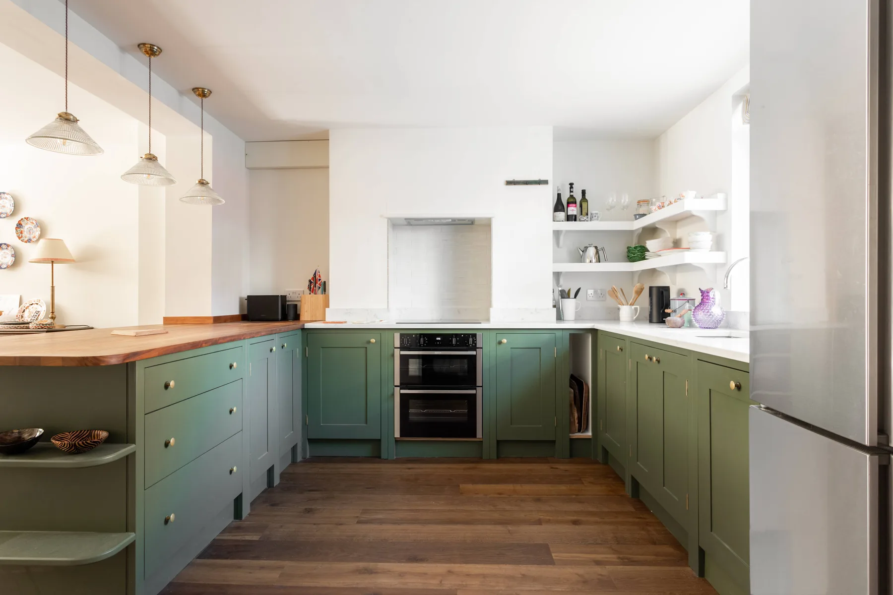 Una cocina luminosa con gabinetes verdes, encimeras de madera y una cocina central.