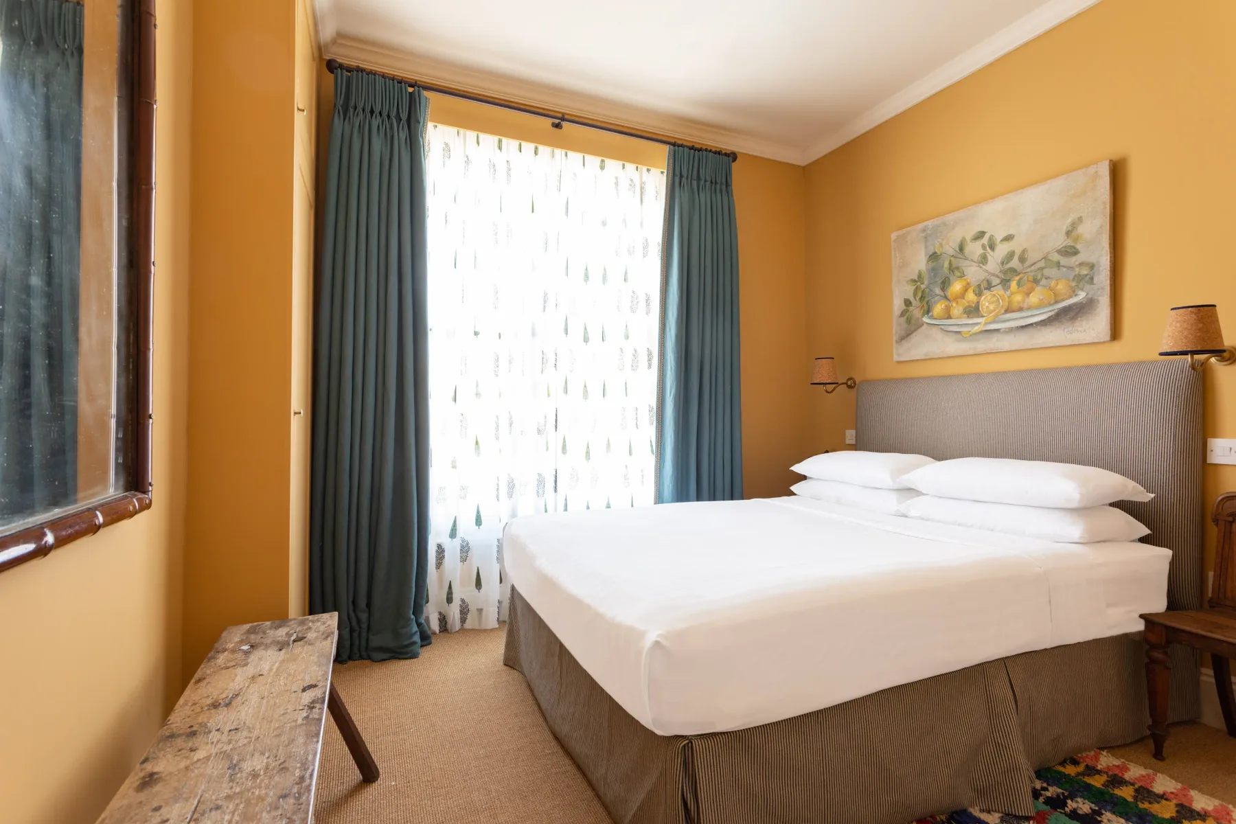 A bedroom with a neatly made bed, teal curtains, and warm yellow walls.