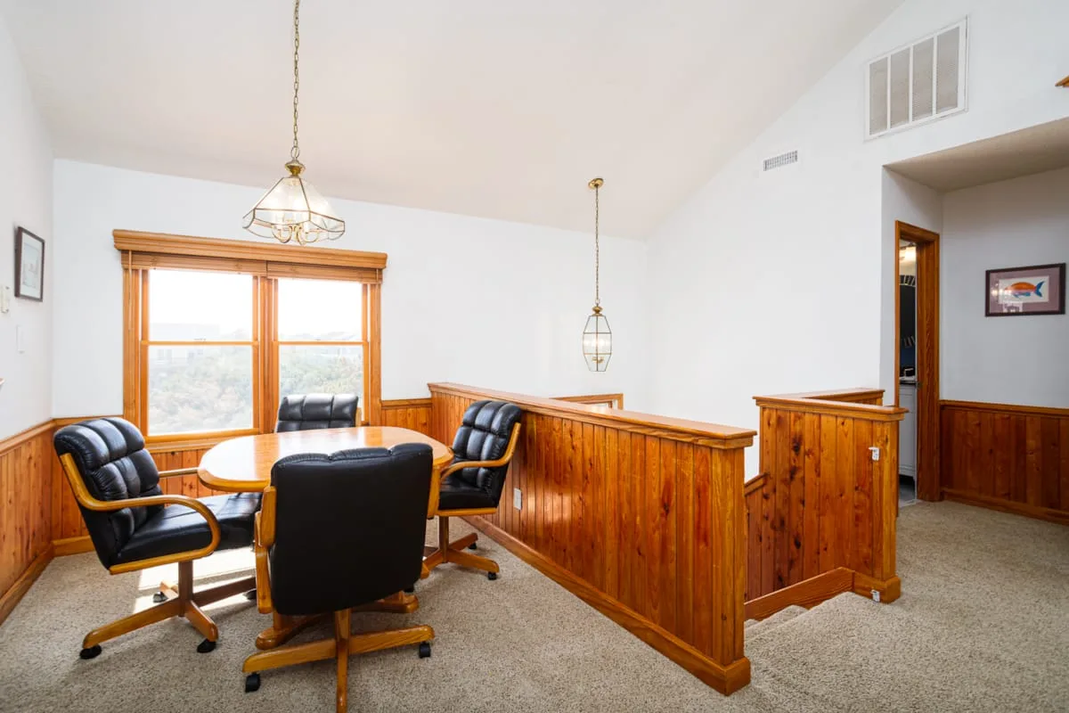 Una habitación alfombrada con asientos negros alrededor de una mesa y paneles de madera.